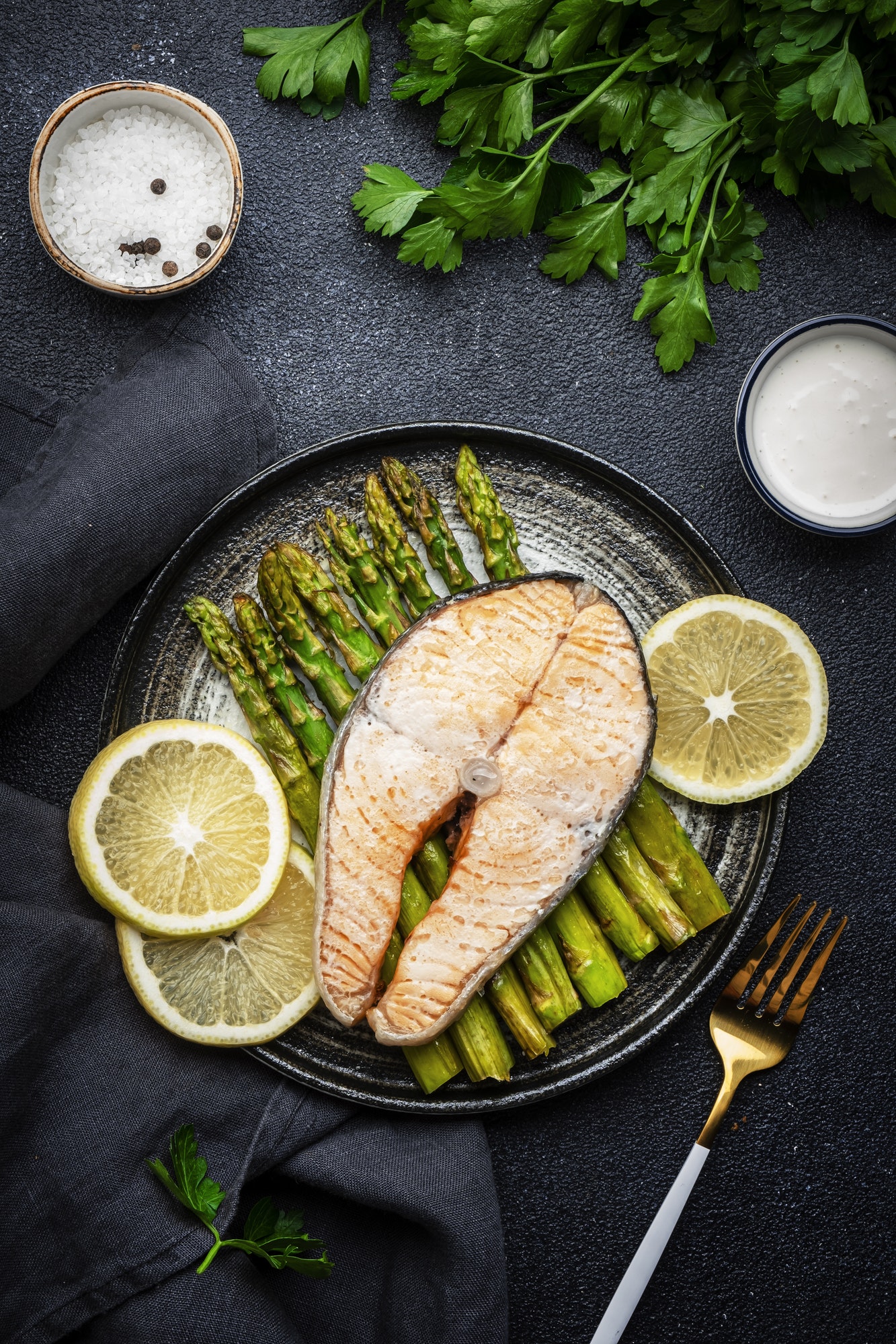 Baked steam salmon with asparagus and lemon with hollandaise sauce on plate.